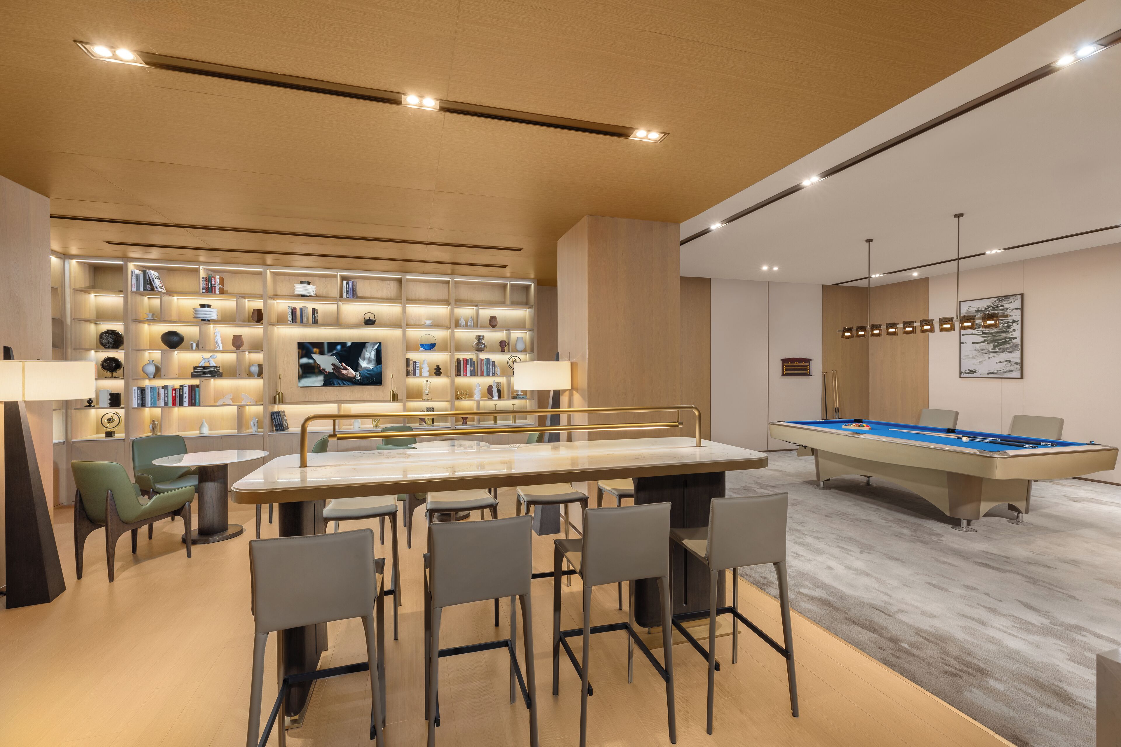 A modern lounge area with a pool table, bar seating, and a bookshelf with various items.