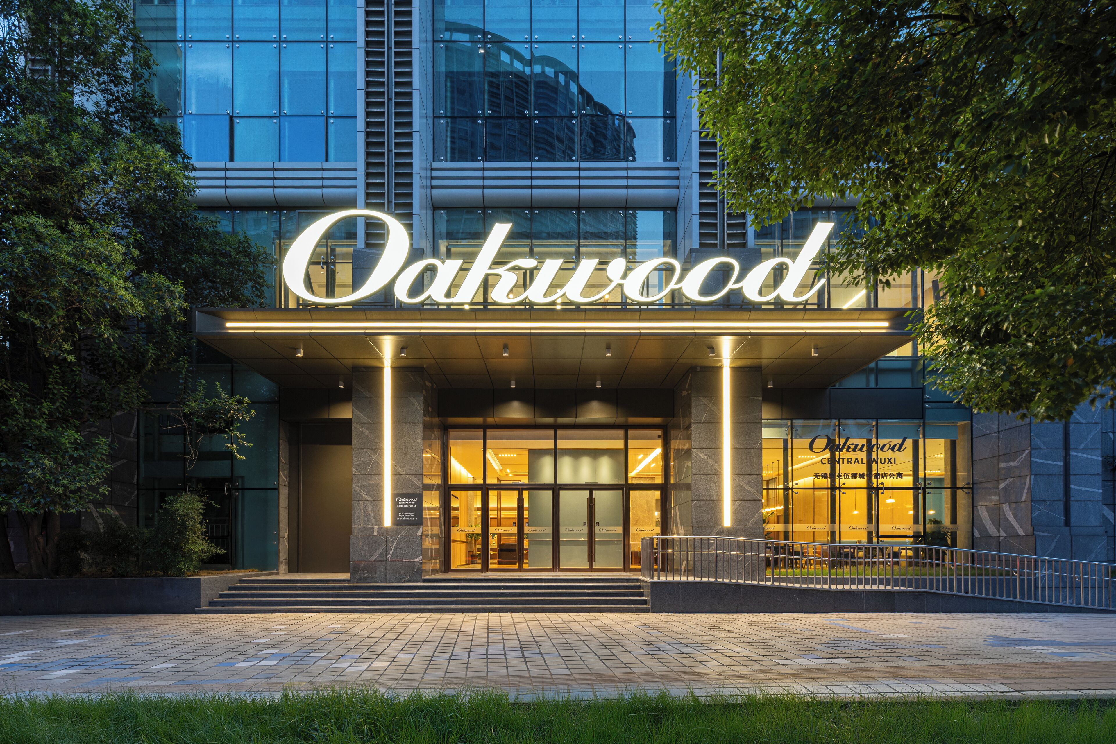 The exterior of the Oakwood Central Hotel with a prominent illuminated sign, a glass facade, and a well-lit entrance.