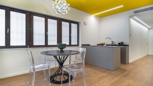 A modern kitchen with a central island, a dining area with a round table and chairs, and large windows with frosted glass.