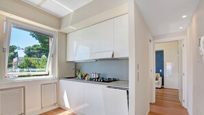 Una cocina moderna con armarios blancos, un ventanal con vista a árboles y piso de madera.