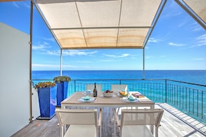 A covered outdoor dining area with a table set for two, overlooking the sea.