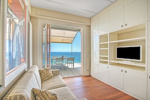 Una sala de estar con sofá, televisor y un balcón con vista al mar.