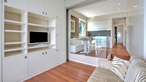 Una sala moderna con un televisor de pantalla plana, muebles blancos y un sofá a rayas.