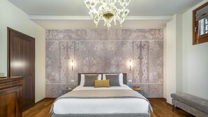 A bedroom with a large bed, a chandelier, two wall-mounted lights, a wooden wardrobe, and a bench. - Domus Carla With Garden R&R (Venecia)