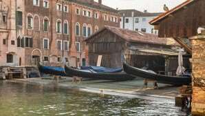 A canal with gondolas docked at a wooden building with a tiled roof. - Domus Carla With Garden R&R (Venecia)