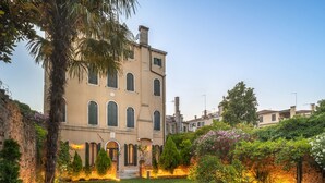 A historic building with a courtyard featuring a well-maintained lawn, a variety of shrubs, and a palm tree. - Domus Carla With Garden R&R (Venecia)