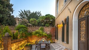 A courtyard with a table and chairs, a brick wall, and a door with decorative ironwork. - Domus Carla With Garden R&R (Venecia)