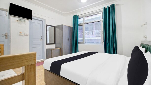 A hotel room with a bed, a chair, a wardrobe, a mirror, and a window with curtains. - Deluxe Hotel New Time Star (Srinagar)