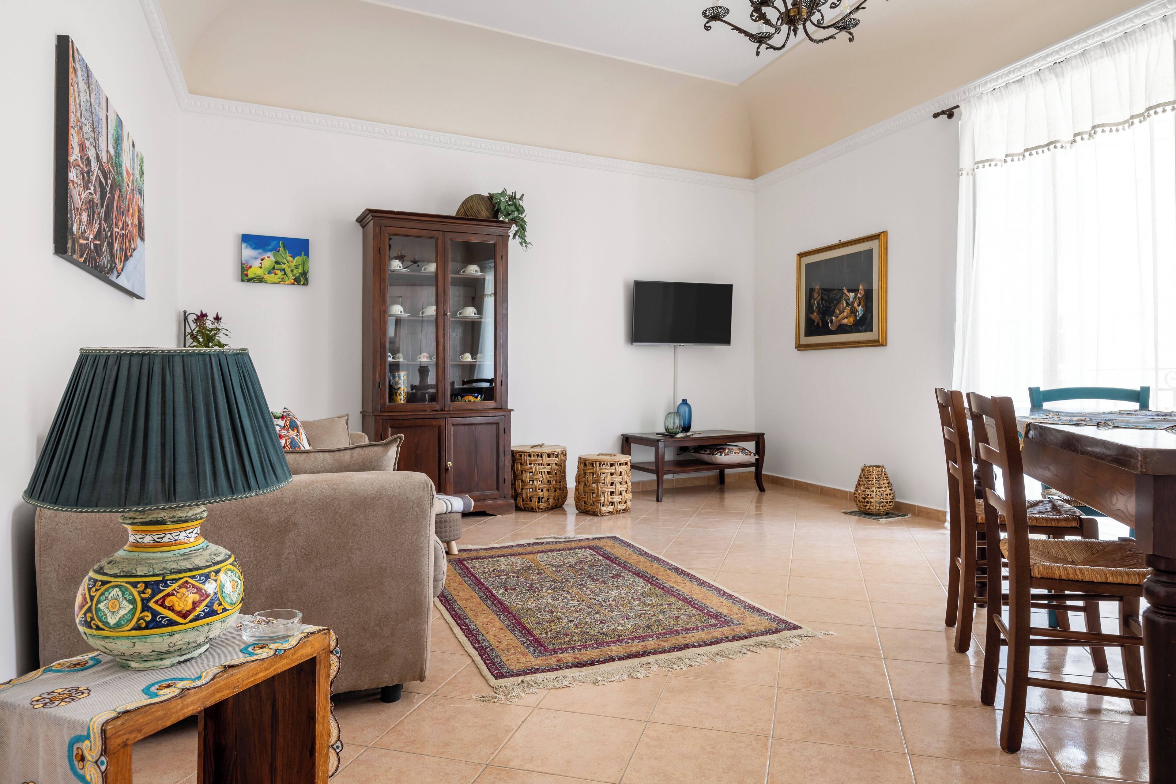 A living room with a sofa, a coffee table, a TV, a dining table with chairs, and a cabinet with glass doors.