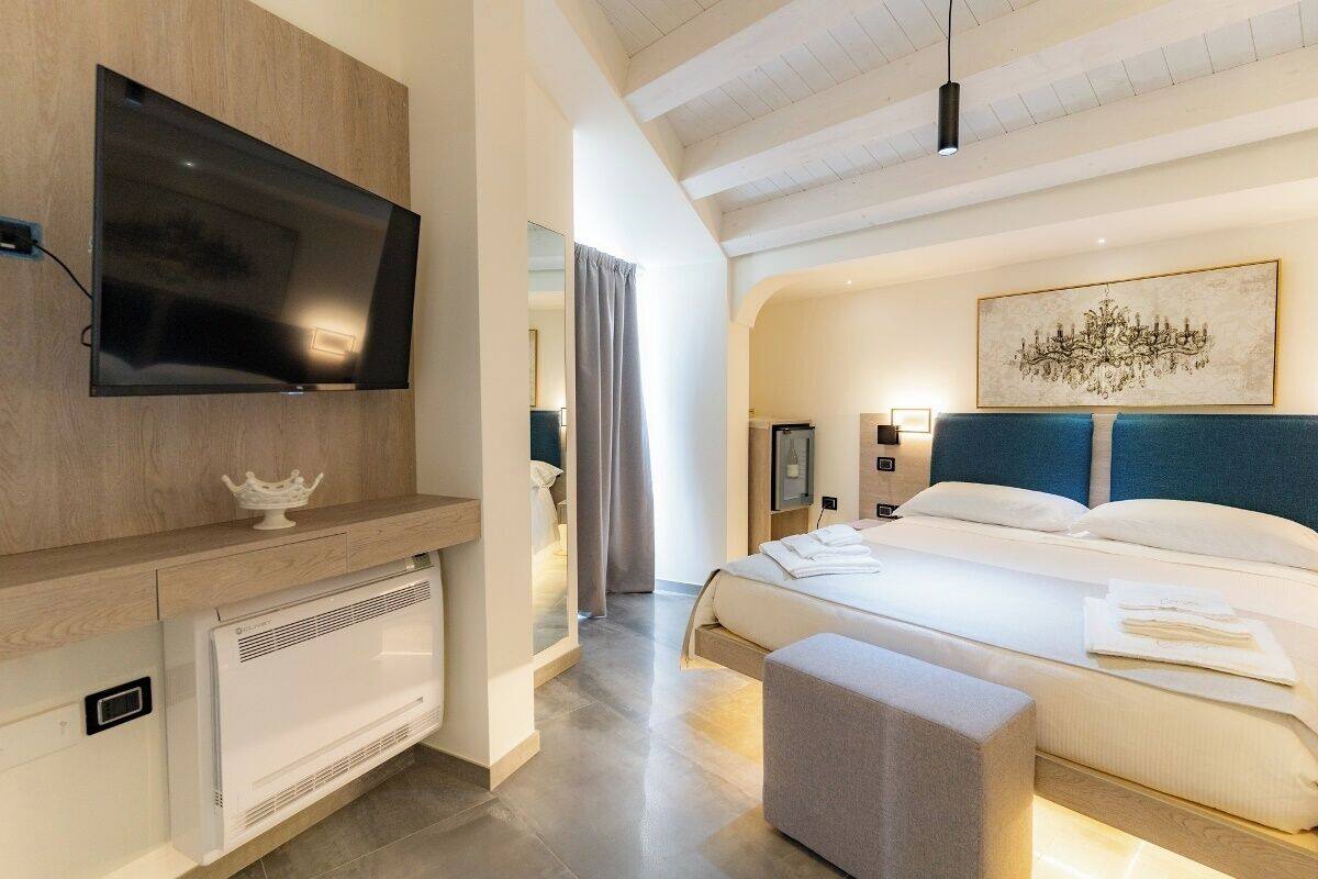 A modern hotel room with a flat-screen TV, a large bed with a blue headboard, a bedside table, and a large painting on the wall.
