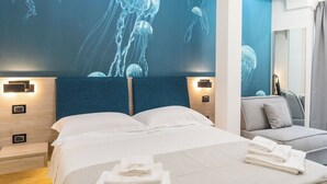 A hotel room with a bed, a sofa, and a wall with a jellyfish mural. - Carizza Rooms (Pozzallo)