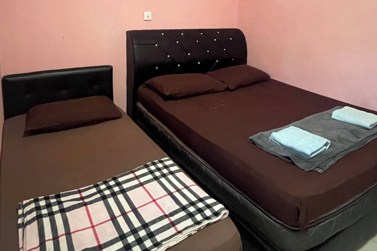 A room with two beds, a wall-mounted light, and a small picture.