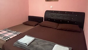 A bedroom with a bed, pillows, a blanket, an air conditioning unit, and a wall-mounted light fixture.