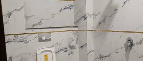 A bathroom with marble walls, a toilet, a shower, and a sink.