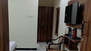 A compact room with a bed, a wooden table, a TV mounted on a wooden cabinet, and a wardrobe. - Hotel The Castle Inn (Varanasi)