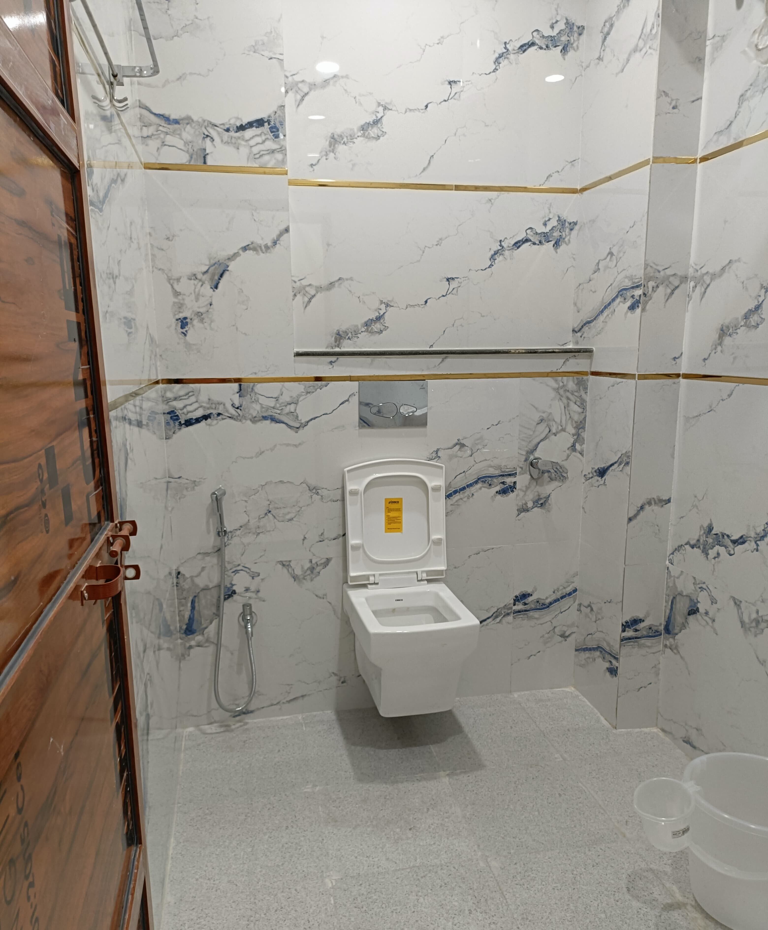 Een badkamer met een wit toilet, marmeren wanden en een houten deur.