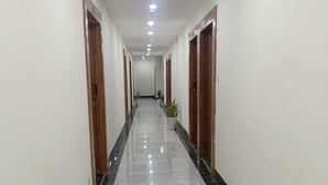 A long, narrow hallway with a polished marble floor, wooden doors on both sides, and potted plants along the walls. - Hotel The Castle Inn (Varanasi)