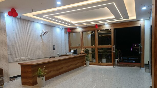 A modern reception area with a wooden reception desk, potted plants, and a large window providing a view of the outside. - Hotel The Castle Inn (Varanasi)