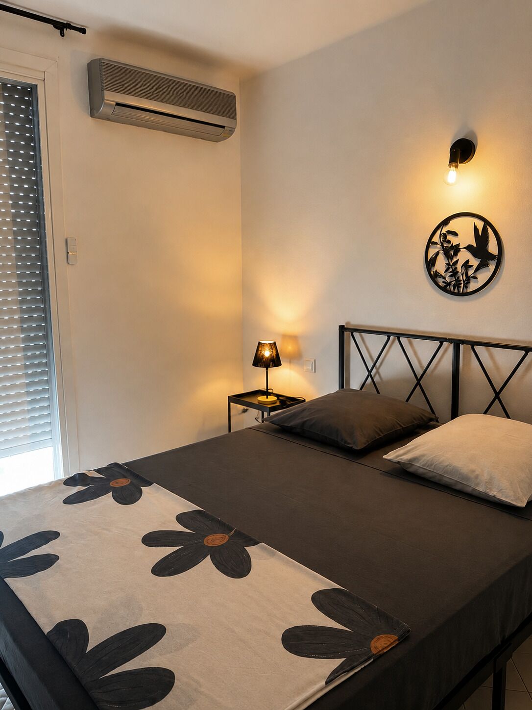 Een slaapkamer met een bed, bedlamp, wandairconditioner en een decoratief kunstwerk aan de muur.