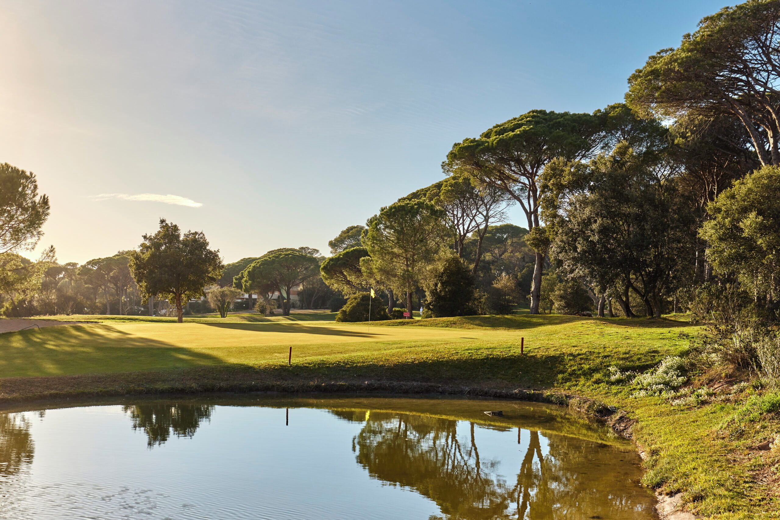 Um campo de golfe tranquilo com um lago refletindo árvores e um céu claro.