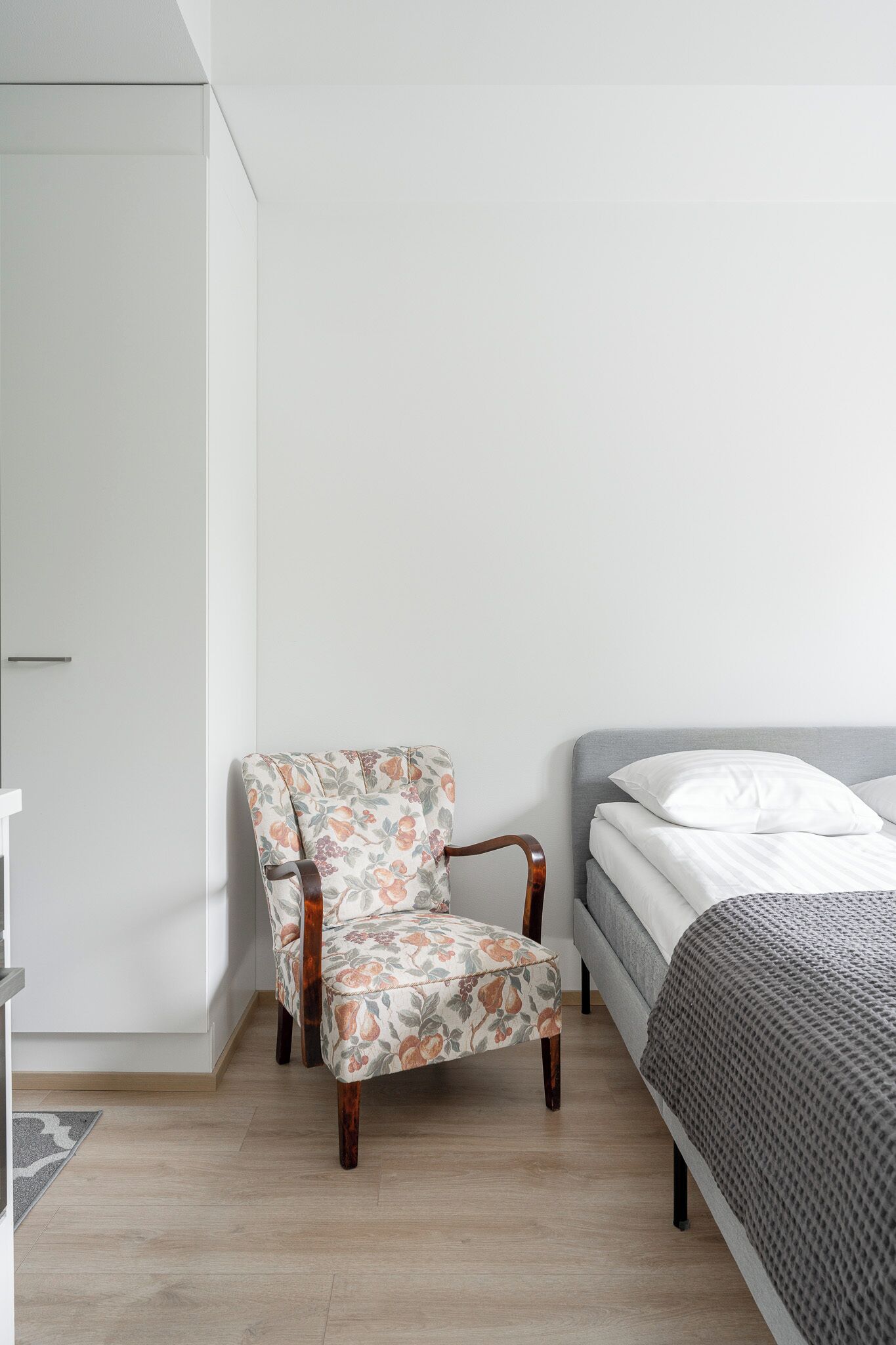 Un dormitorio con cama, una silla con tapicería floral y piso de madera.