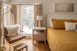 A bedroom with a bed, a chair, a nightstand, a lamp, and a window with curtains. - Game Room | Hot Tub | Near Skiing (Big Sky)