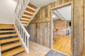 A wooden staircase with white railings leading to a room with a brick wall and a wooden floor.
