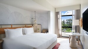 Habitación de hotel con una cama grande, una mesita con lámpara, televisión y vistas a zonas verdes por la ventana.