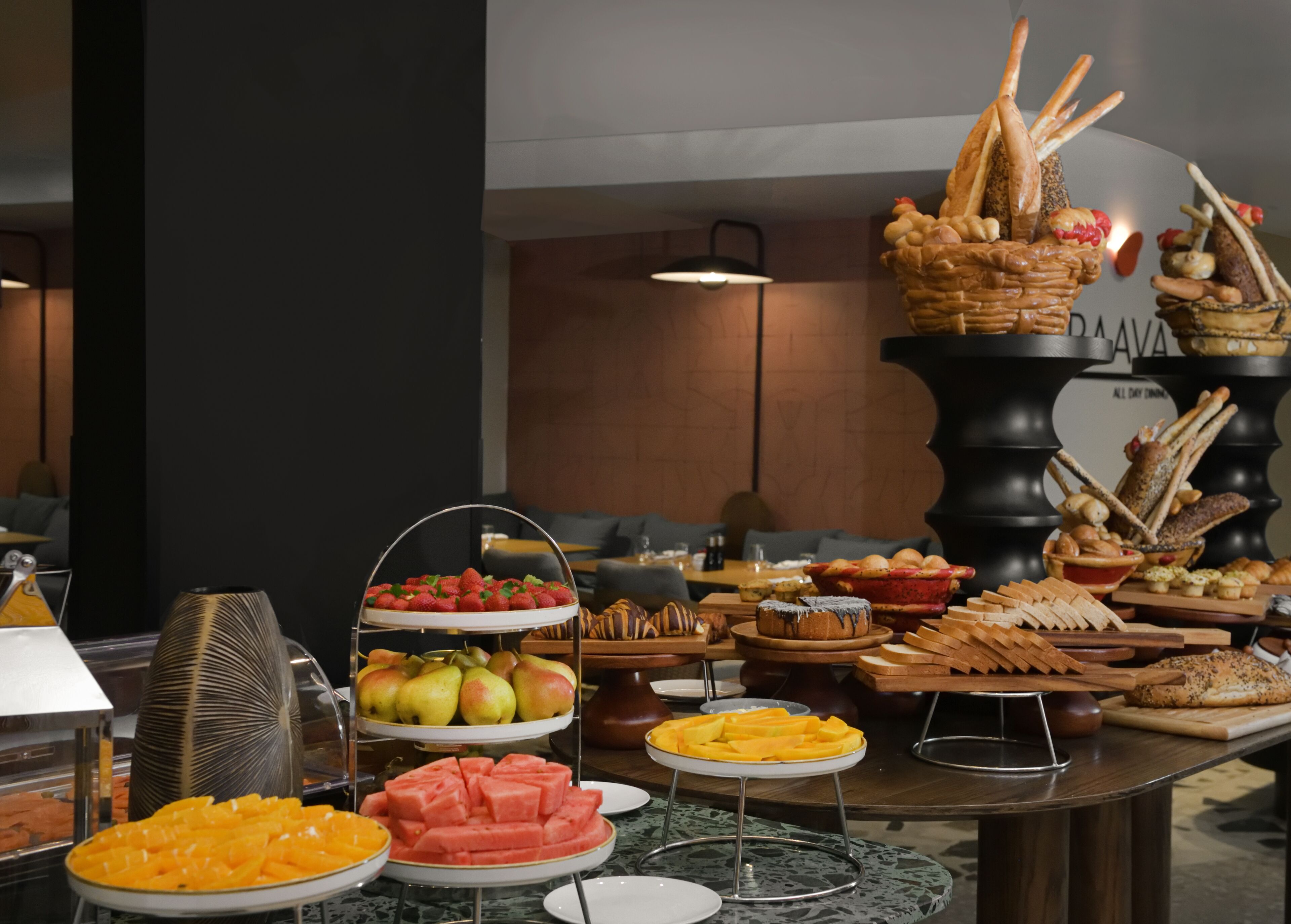 A buffet with various food items including fruits, pastries, and bread.