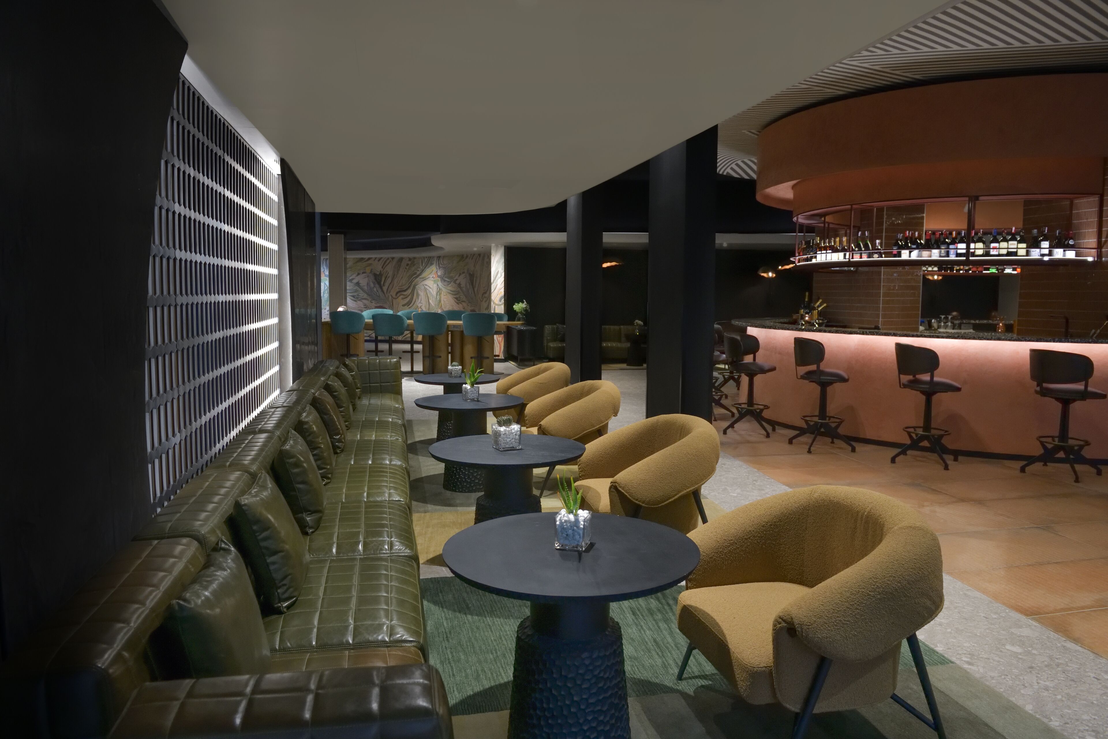 A modern lounge area with leather sofas, round tables, and a bar with a curved design.