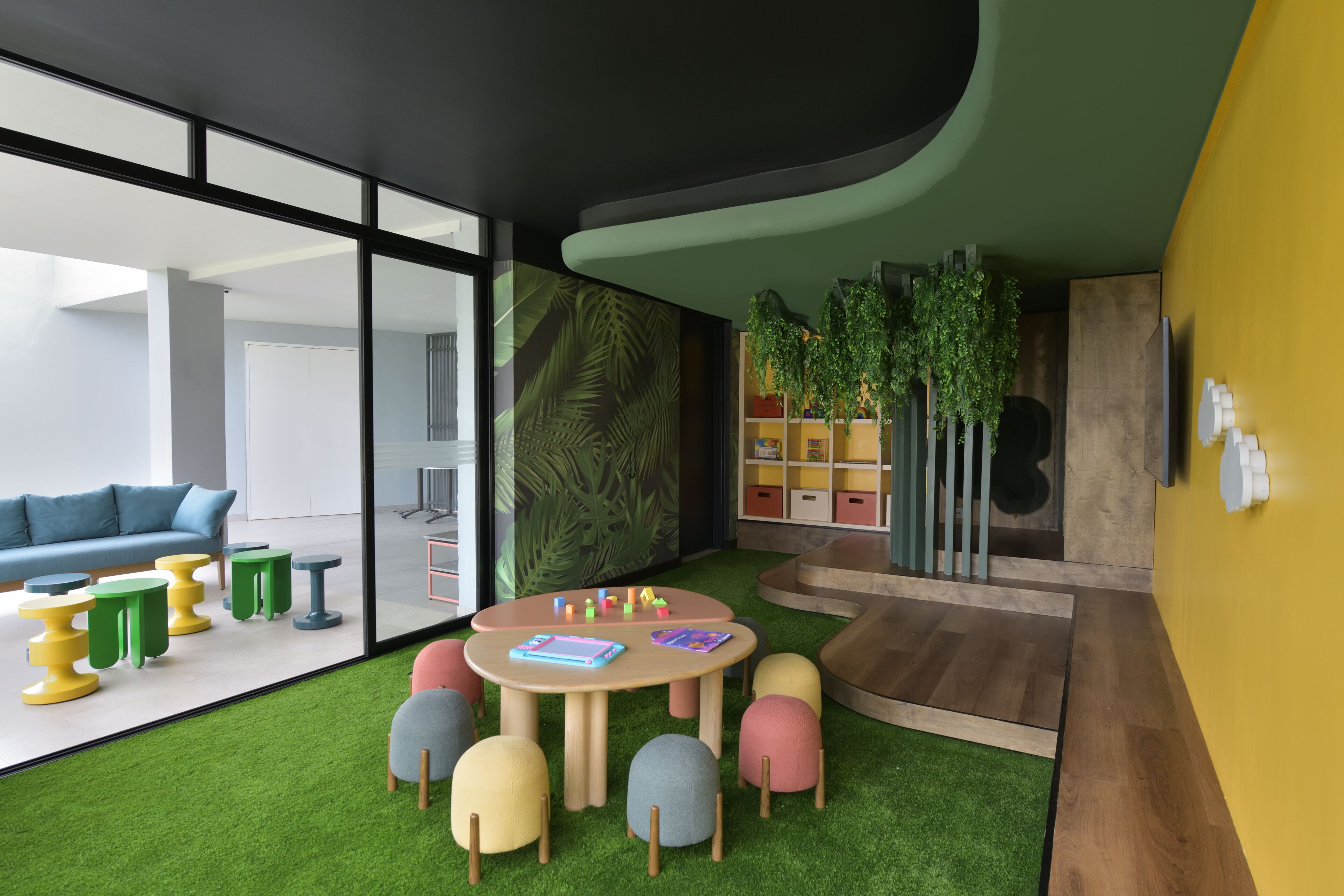 Un intérieur moderne avec une table ronde, des tabourets colorés, un canapé bleu et un mur vert orné de plantes.