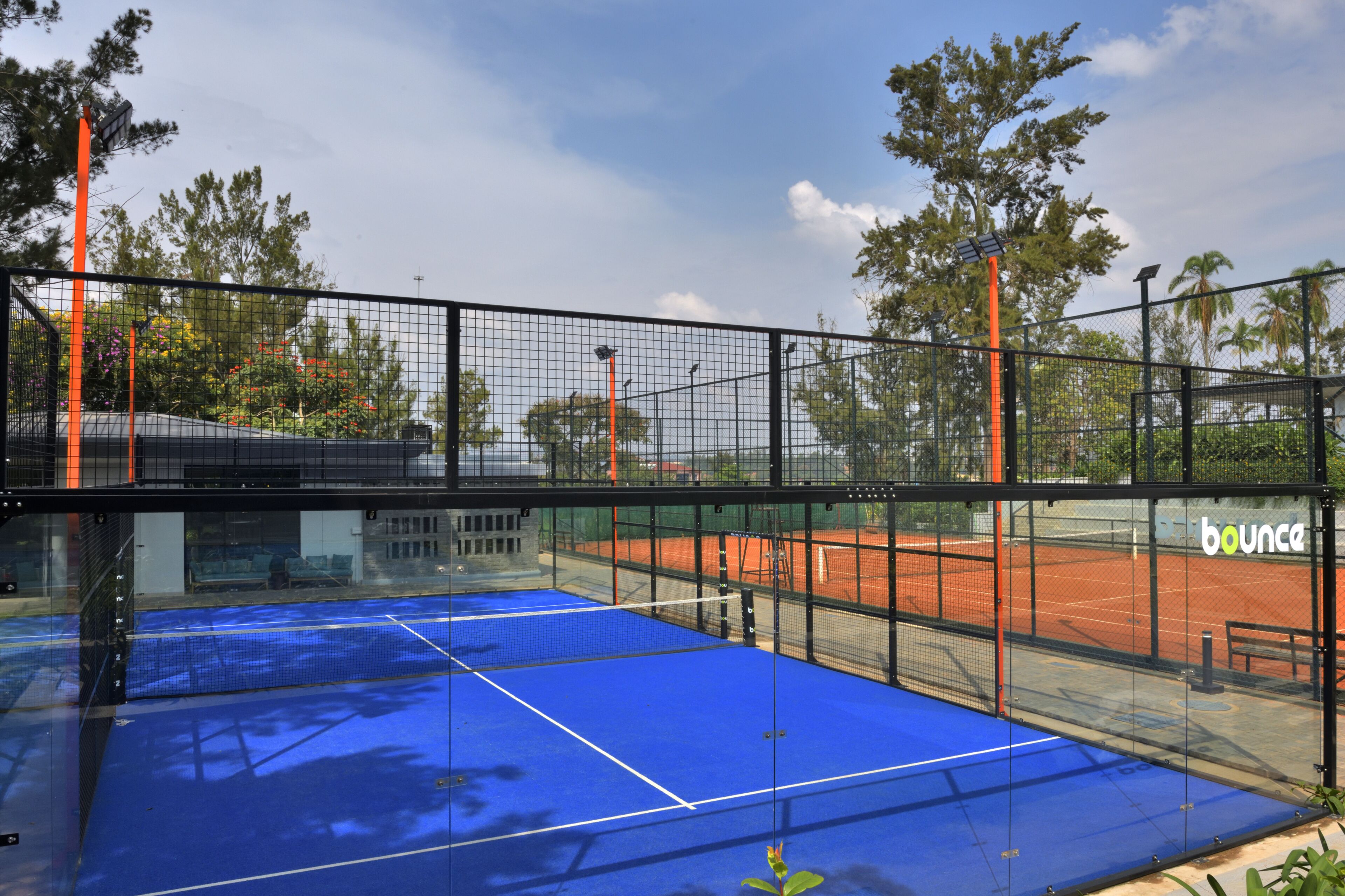 Una cancha de tenis con red, rodeada por una valla, y un banco al fondo.