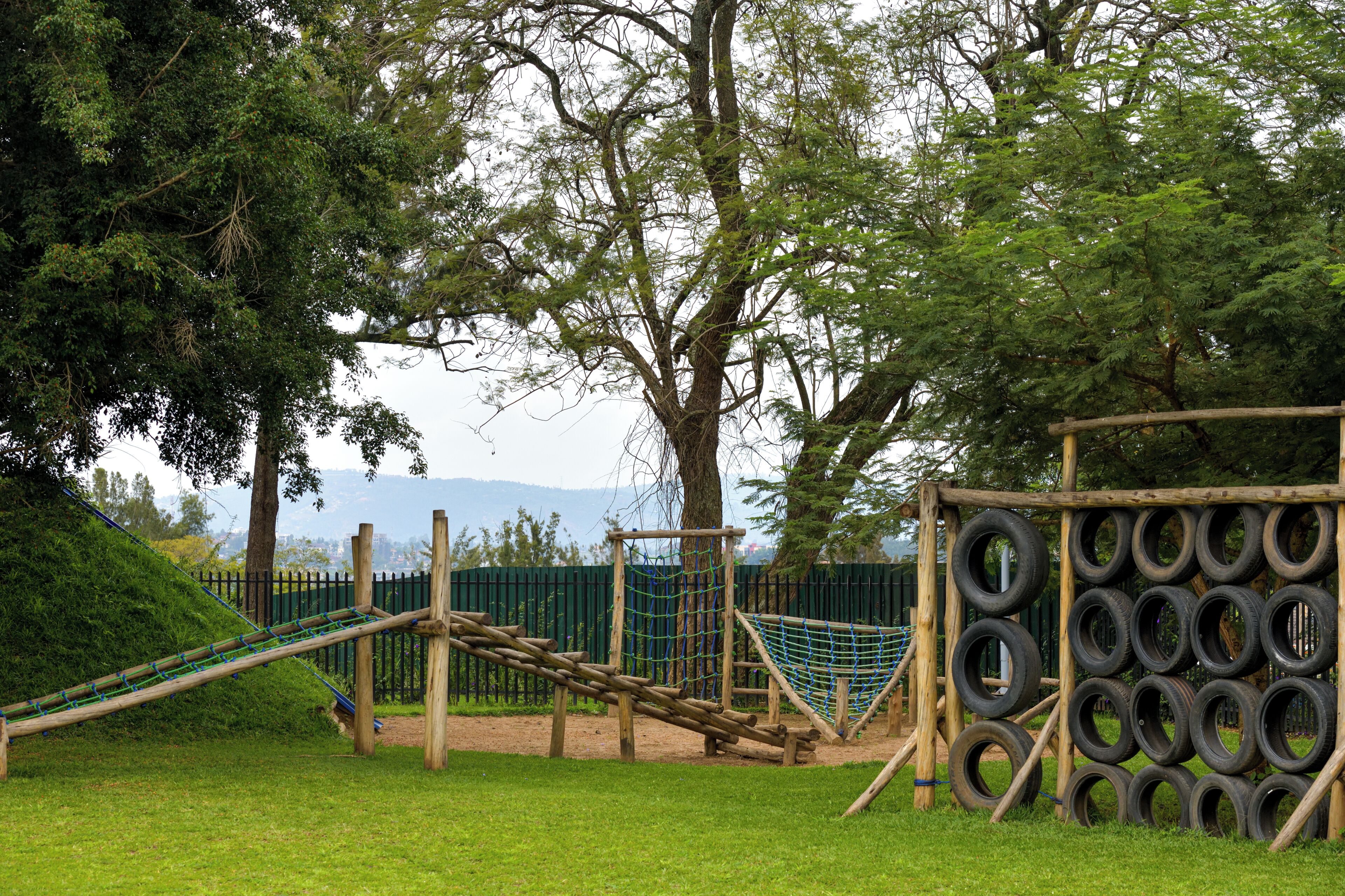 A playground with a rope bridge, tire climbing wall, and a slide.