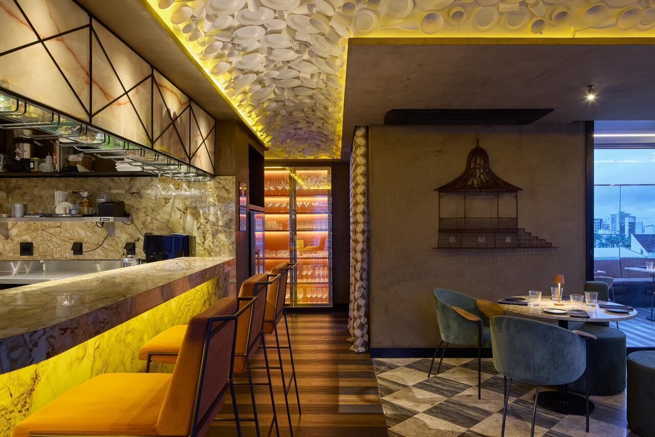 Zona de bar moderna amb taulell de marbre, tamborets i sostre amb un disseny