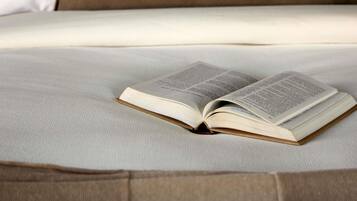 An open book on a bed with a plain white sheet and a brown pillow.