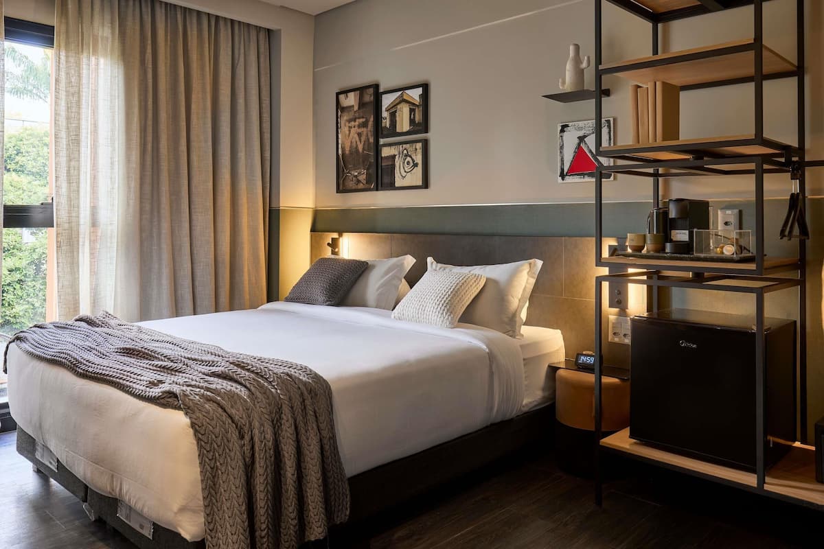 A modern hotel room with a bed, bedside tables, a built-in TV, and a shelf with amenities.