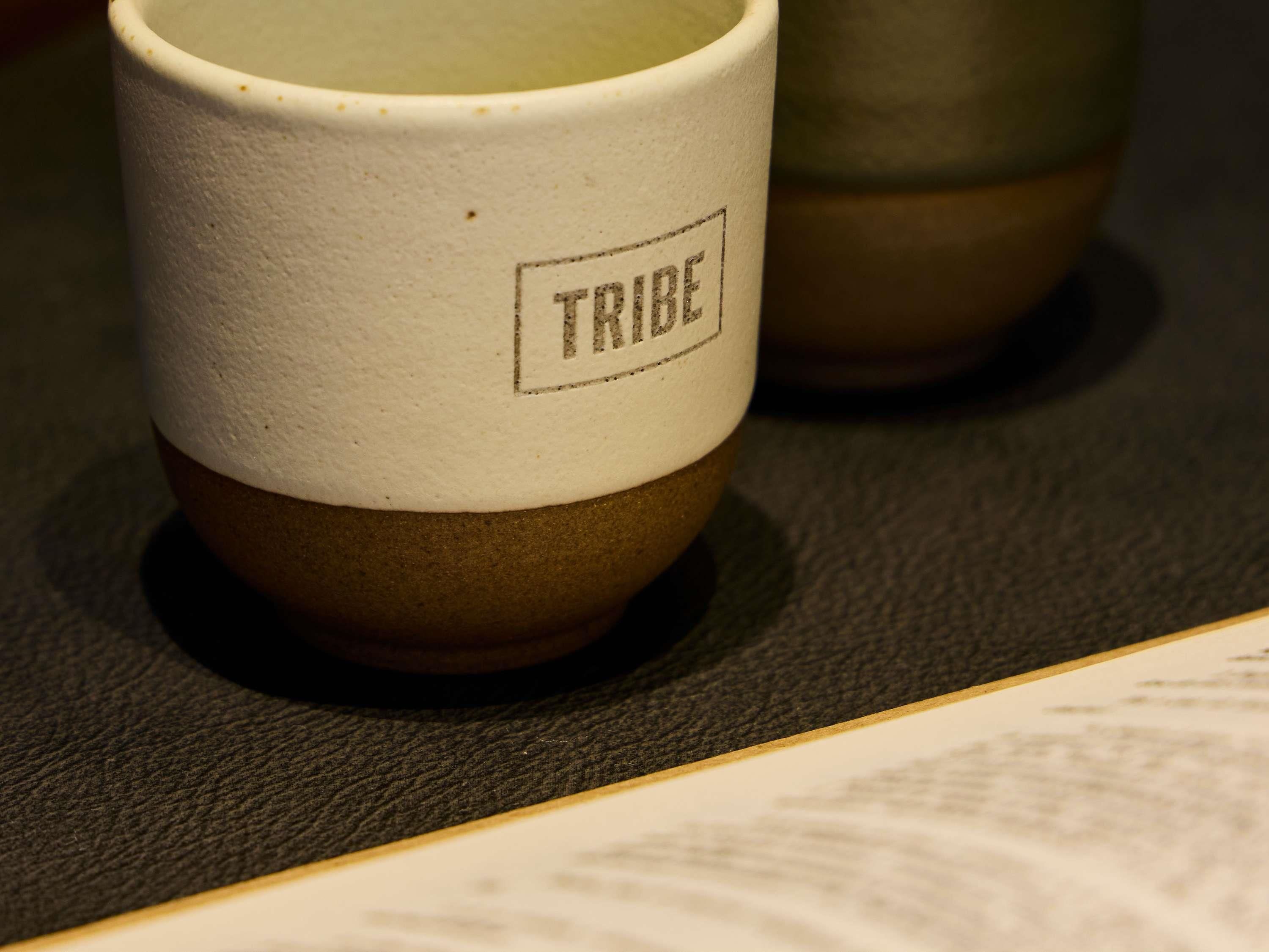 A close-up of a ceramic mug with the word 'TRIBE' on it.