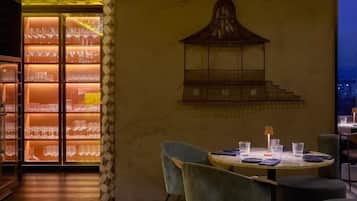 Interior de restaurante com teto estampado, obra de arte com gaiola de pássaro na parede e área de refeições com mesas e cadeiras redondas.