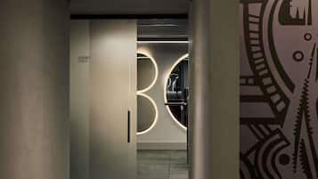 Un pasillo con un cartel que dice 'ACADEMIA FITNESS', una lámpara circular y un revestimiento de pared con diseño.