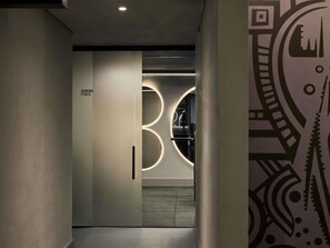 Passadís amb un senyal que diu 'ACADEMIA FITNESS', una il·luminació circular i un mur amb un disseny.