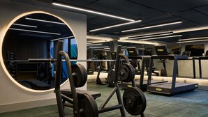 Un gimnasio con equipo de levantamiento de pesas, cintas de correr y un espejo grande.