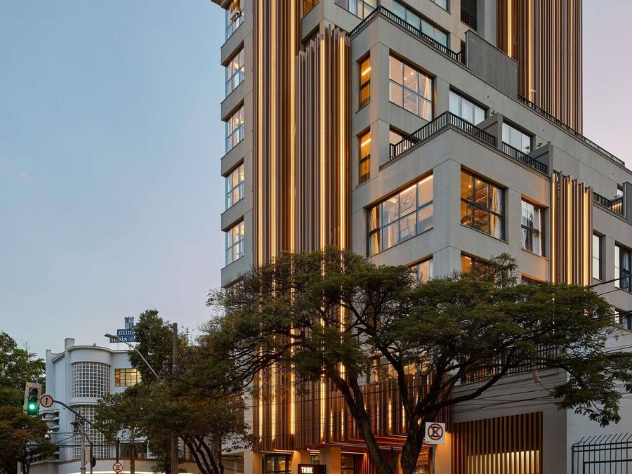 Um edifício moderno de grande altura, com vários andares, janelas amplas e uma marcante estrutura de iluminação vertical.