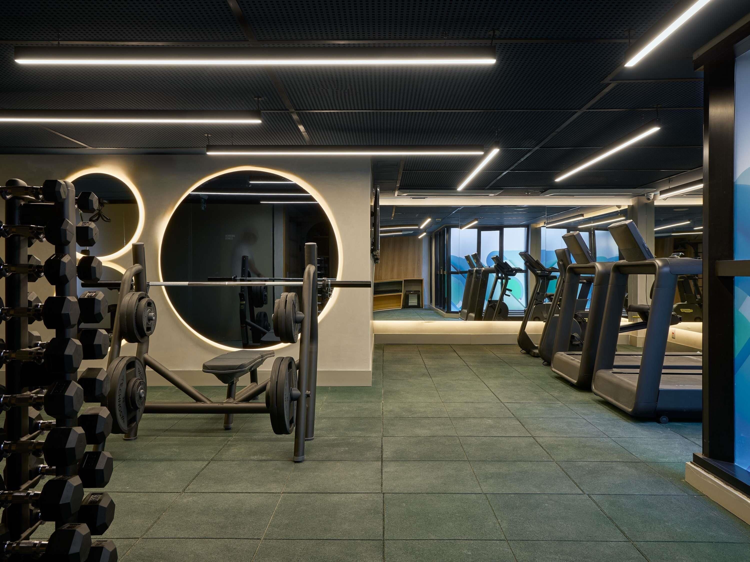 Ein Fitnessraum mit Gewichte, Laufbändern und einem großen runden Spiegel.