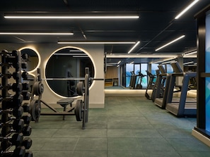 A gym with weightlifting equipment, treadmills, and a large circular mirror. - Tribe Belo Horizonte Savassi (Belo Horizonte)