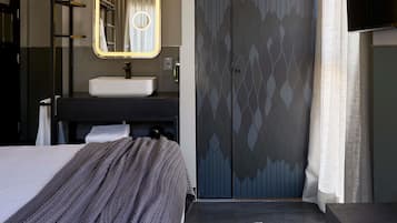 Una habitación de hotel moderna con una cama, un baño con lavamanos y espejo, y un armario.