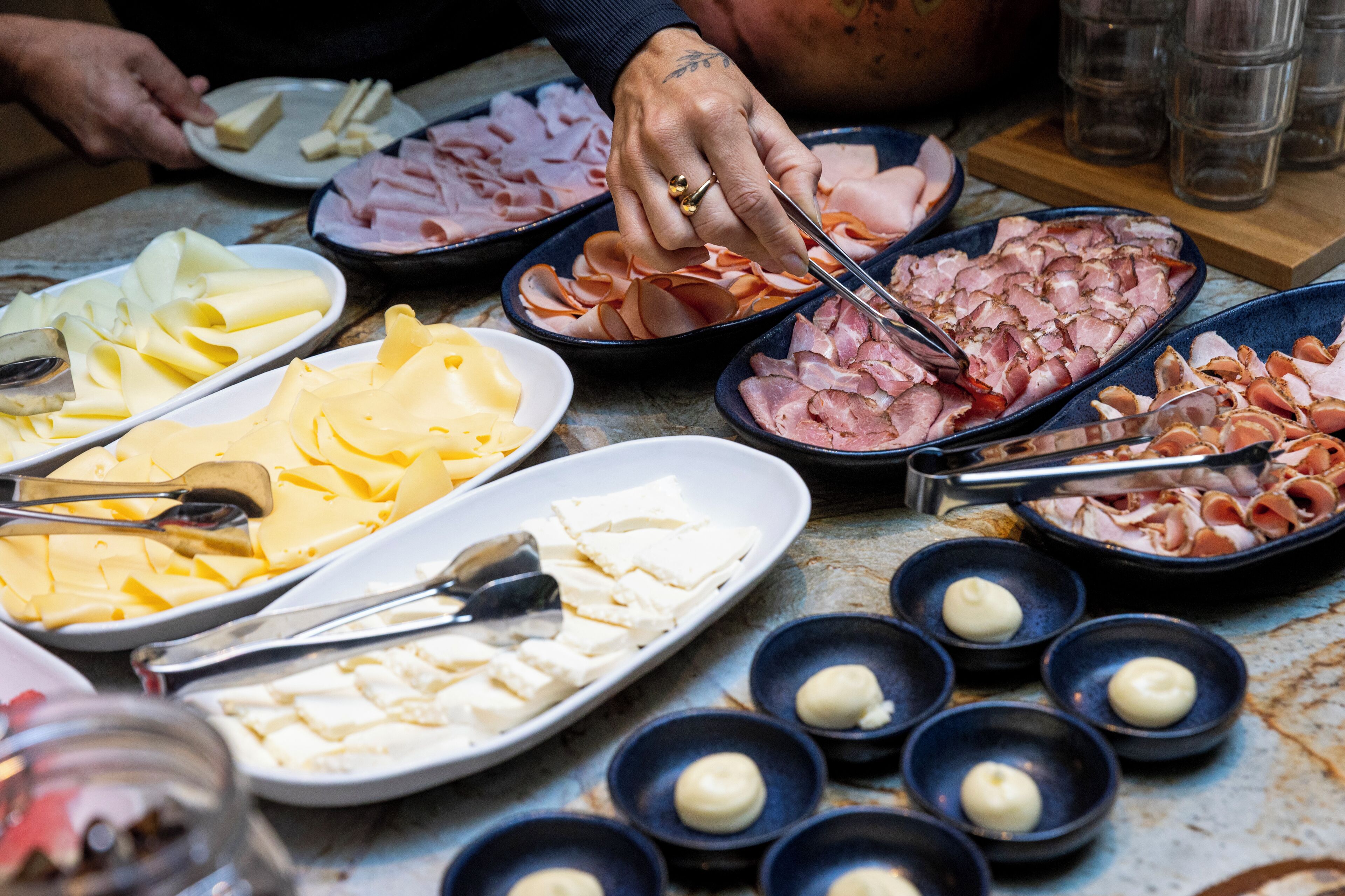 Diversos quesos y embutidos dispuestos sobre una mesa, junto a pequeños recipientes de salsas y aderezos.