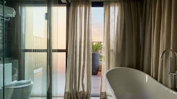 Un baño moderno con una bañera independiente, una ducha con cerramiento de vidrio y vistas a un balcón con cortinas.
