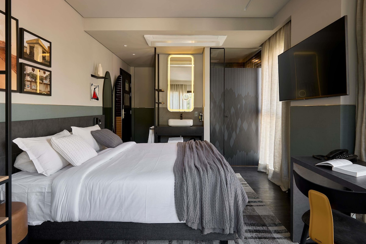 Een moderne hotelkamer met een groot bed, een bureau met stoel, een televisie en een badkamer die door een open deur zichtbaar is.