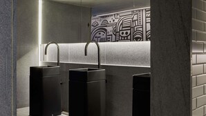 Des toilettes modernes avec des lavabos et des poubelles noirs, un mur carrelé et un luminaire.