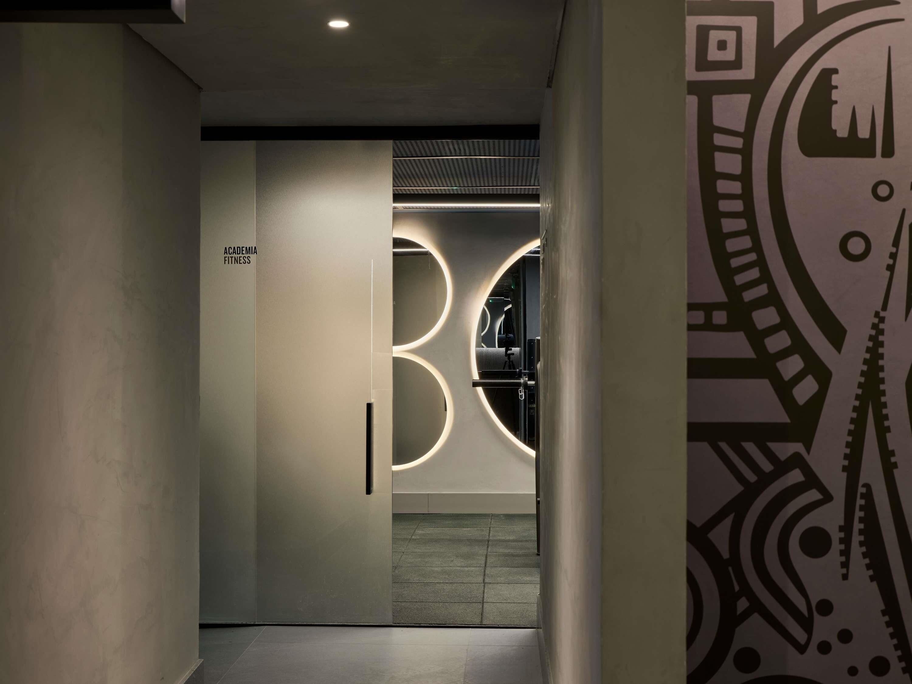 Um corredor com uma placa indicando 'ACADEMIA FITNESS' e um aparelho de iluminação circular.